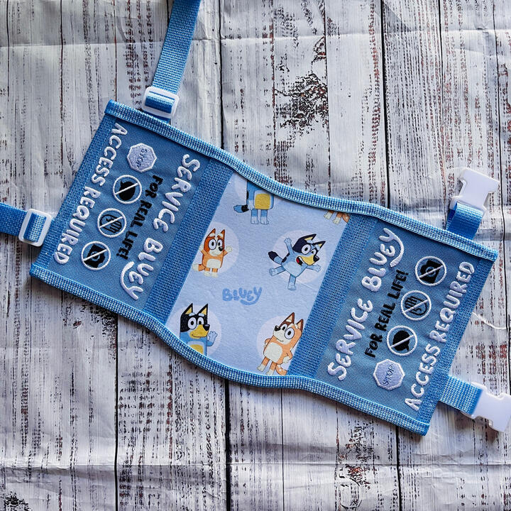 An orange and pink service dog vest with printed fabric featuring Bingo from the cartoon Bluey. Text on the side panels reads: "Service Bingo, cheese and crackers do not pet"